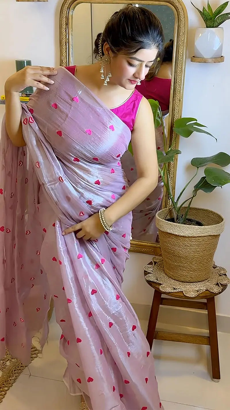 Woman in a pink saree with heart patterns standing in front of a mirror.