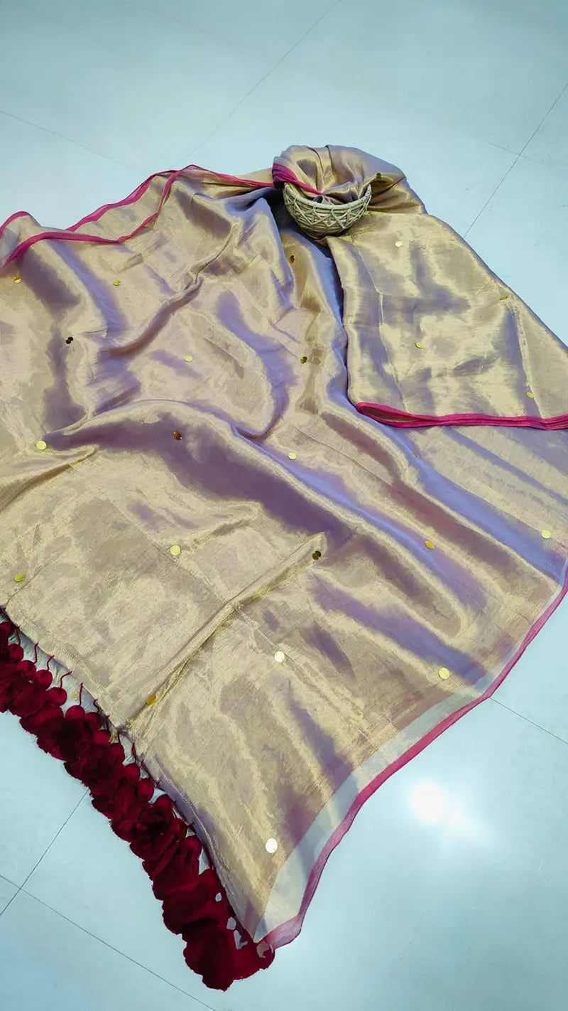 GOld colored tissue saree with red tassels on a light gray floor