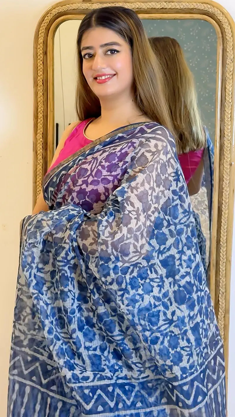 Woman wearing a blue and white floral saree in front of a mirror.