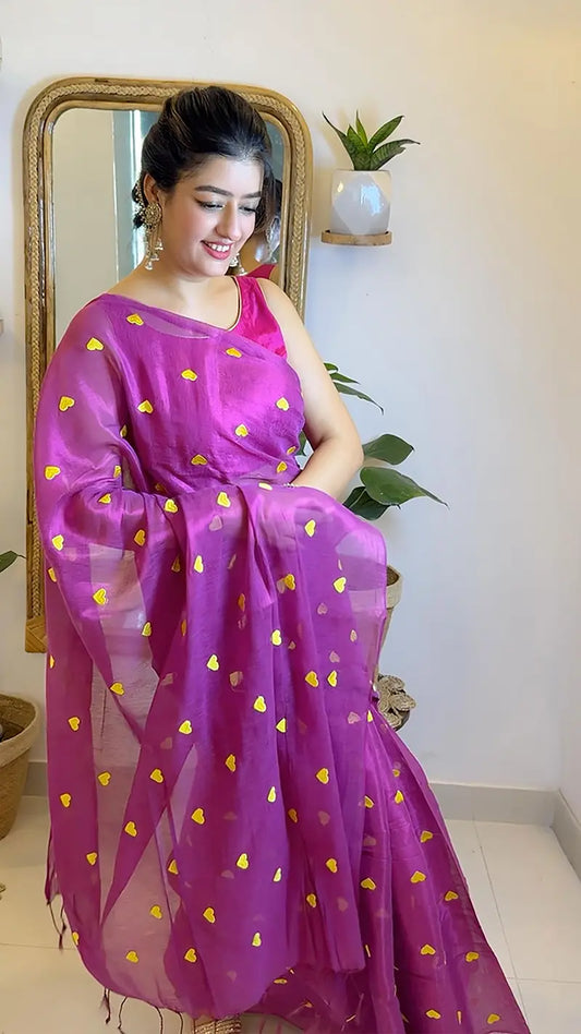 Woman wearing a pink saree with yellow heart patterns, standing indoors.