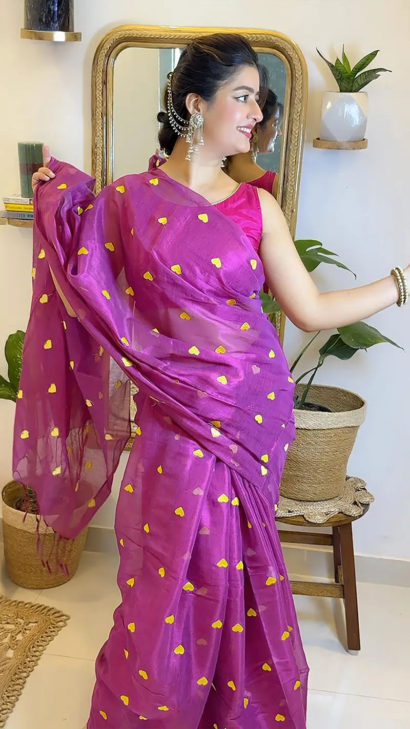 Woman wearing a pink saree with yellow patterns in a room with plants and a mirror.
