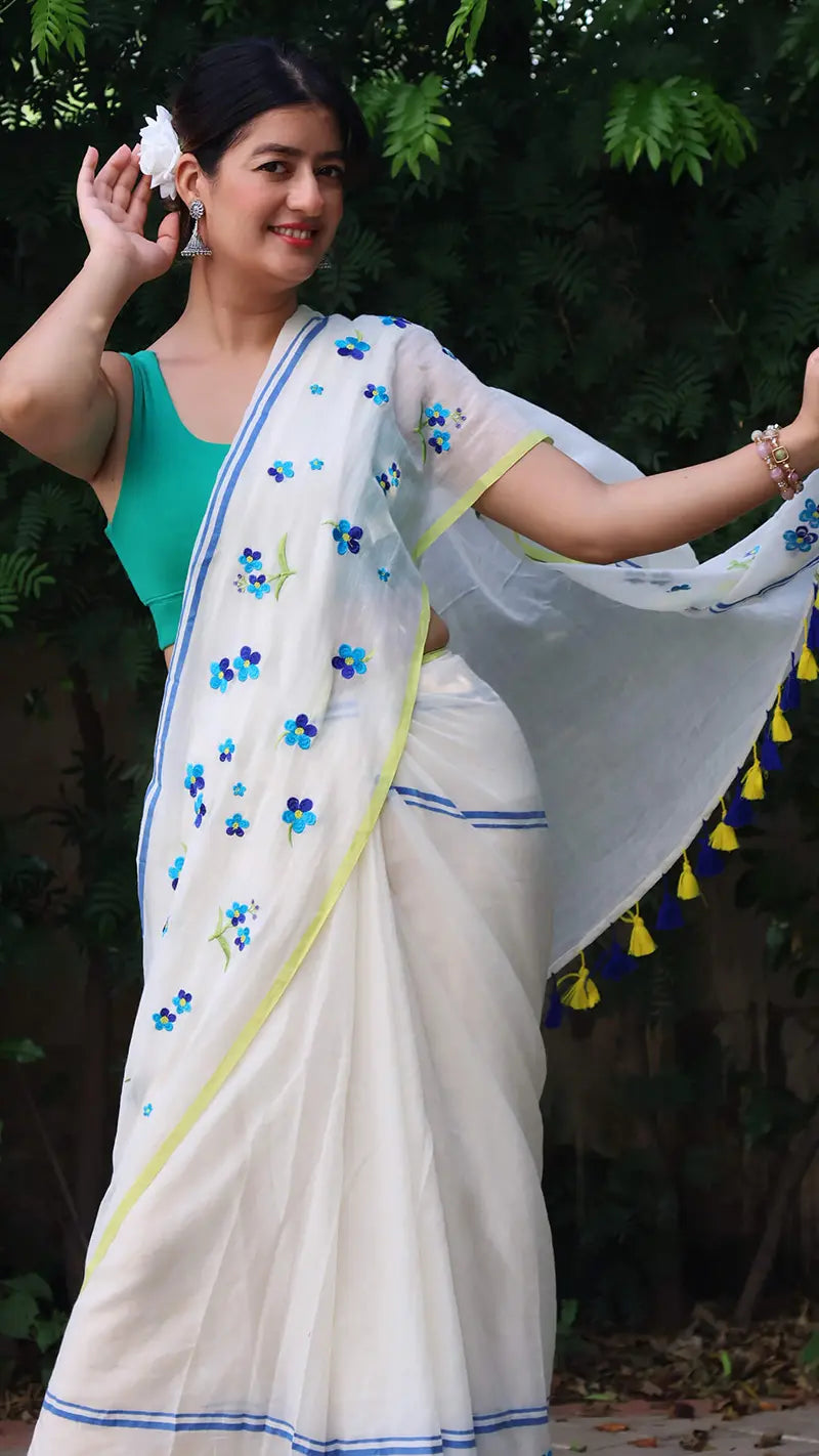 Woman wearing a white saree with blue floral patterns in an outdoor setting
