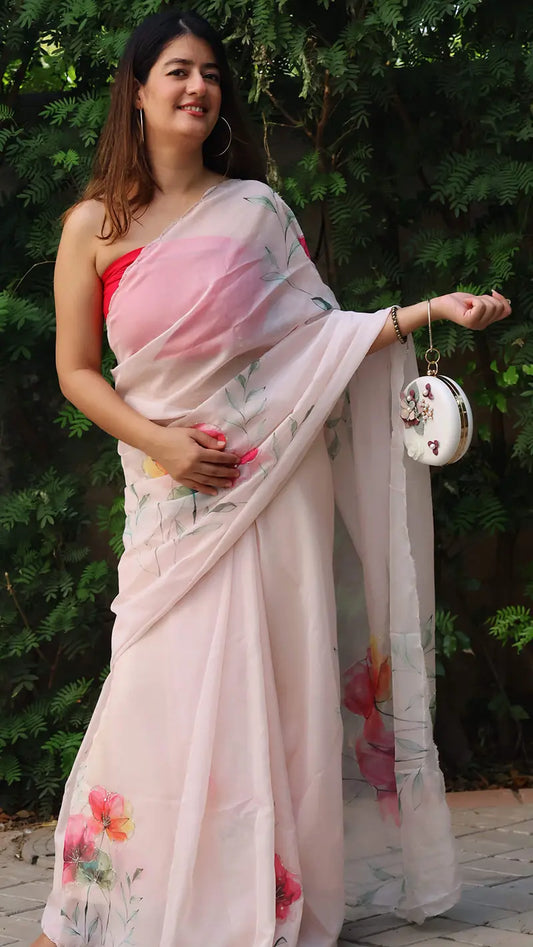 Woman wearing a light pink saree with floral patterns against a green leafy background