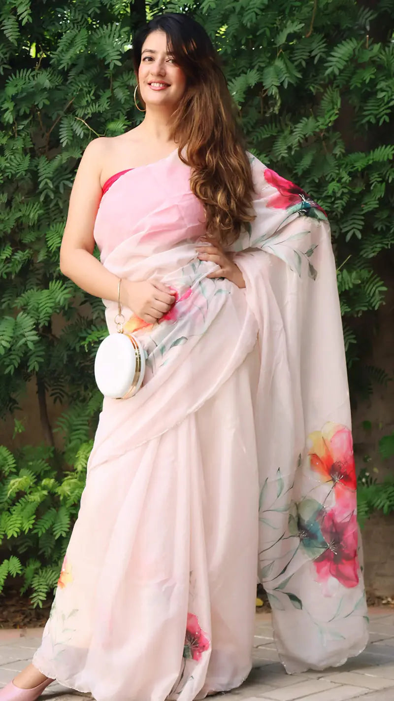 Woman in a floral saree standing outdoors with greenery in the background