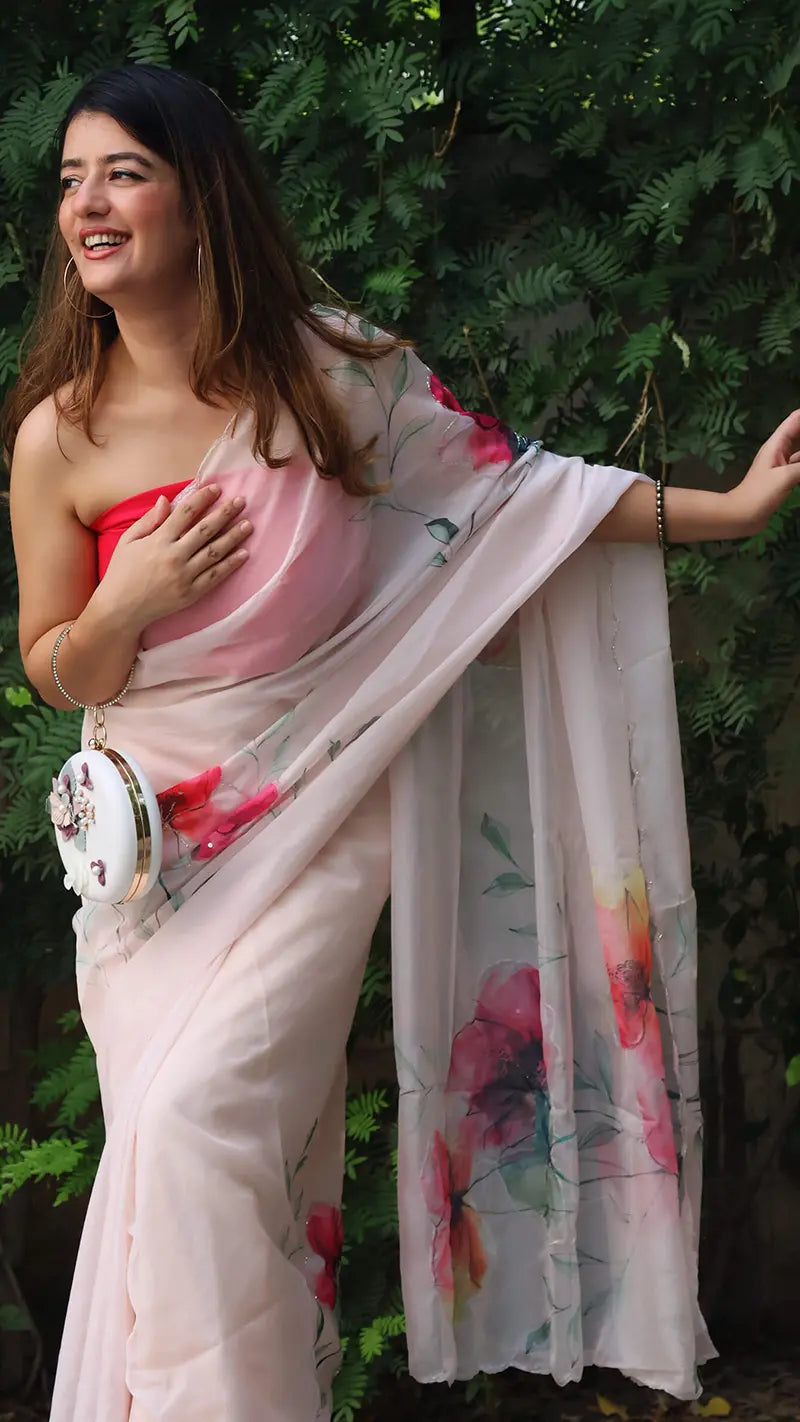 Woman in a white saree with floral patterns standing against a green leafy background